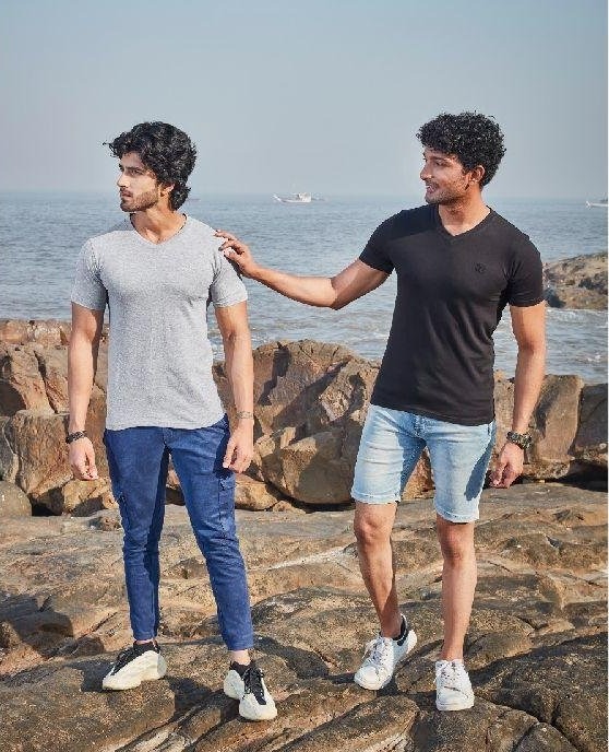 Two men on the rocks by the sea wearing grey and black V-neck T-shirts with denim